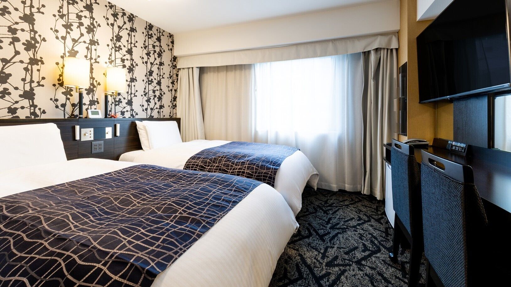 Een hotelkamer met twee bedden, een flatscreen televisie, een bureau en een groot raam met gordijnen.