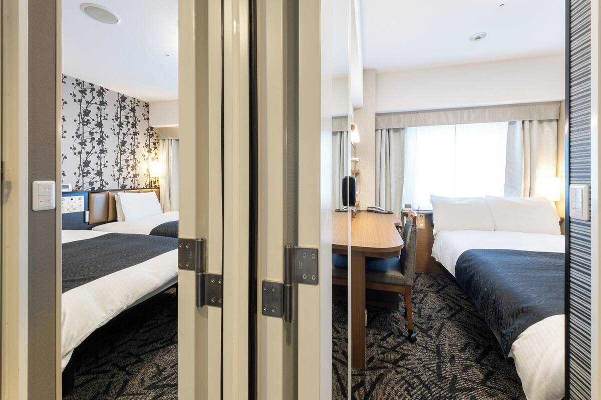 A hotel room with two beds, a desk, and a window with curtains.