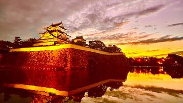 Um castelo japonês tradicional com muro de pedra e reflexo na água, sob um céu nublado.