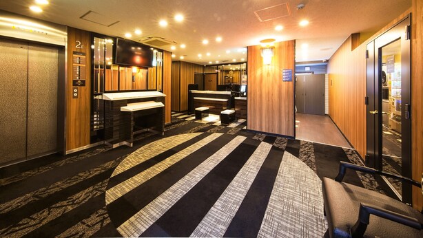 Un vestíbulo de hotel con un mostrador de recepción, una zona de estar y un pasillo que conduce a los ascensores.