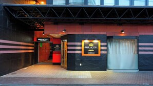 La entrada al APA HOTEL con un diseño moderno, que incluye una zona de recepción y un ascensor de vidrio.