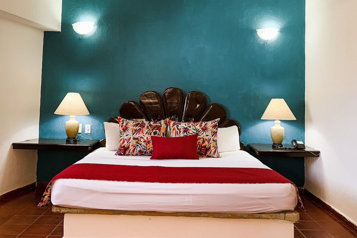 Een hotelkamer met een bed, een plafondventilator, twee nachtkastjes met lampen, en een wand in turquoise.