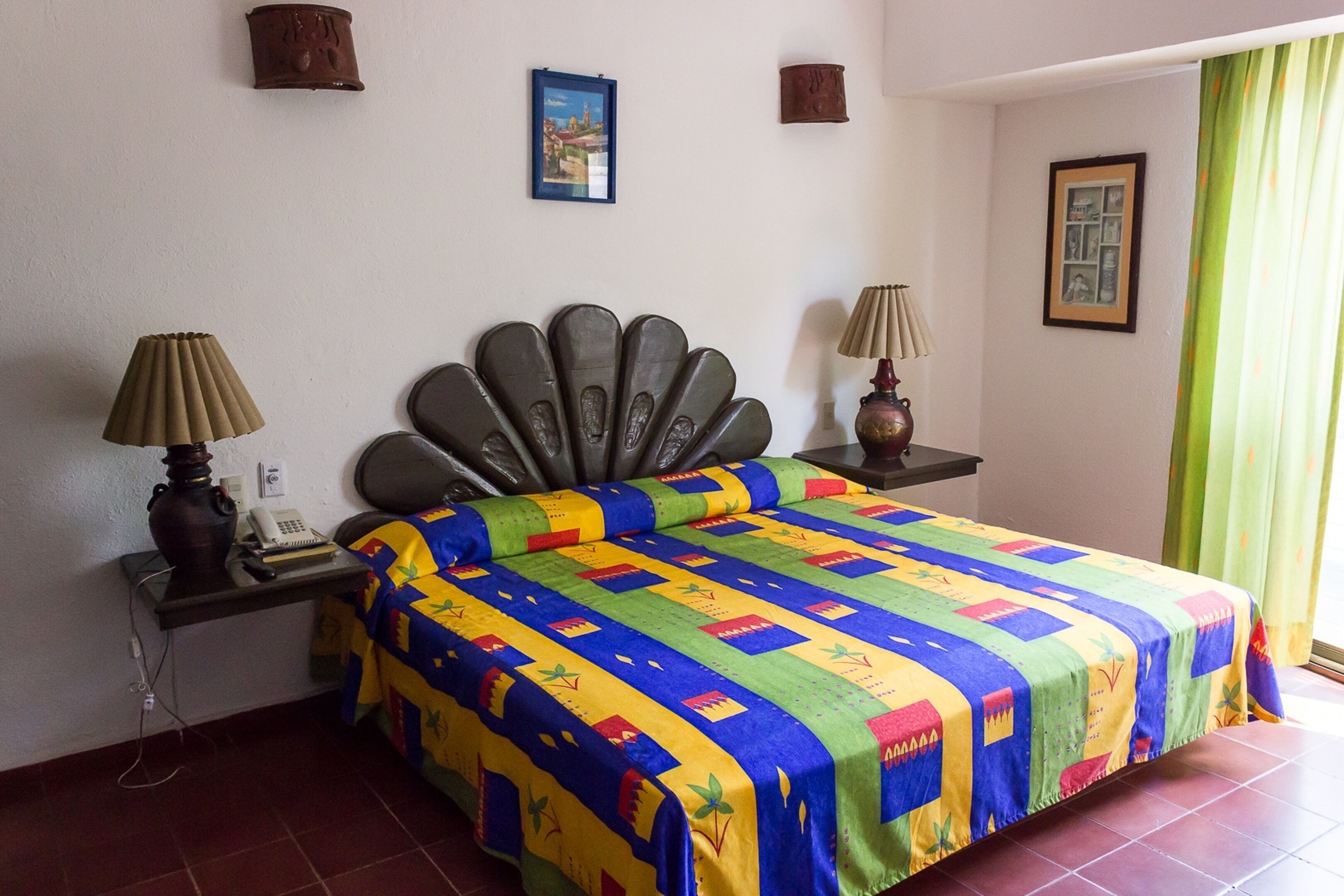 Une chambre d’hôtel avec un lit, deux tables de chevet, une lampe et une fenêtre avec des rideaux.
