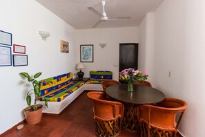 Un coin repas avec une table ronde, des chaises orange, une plante en pot et un canapé coloré.