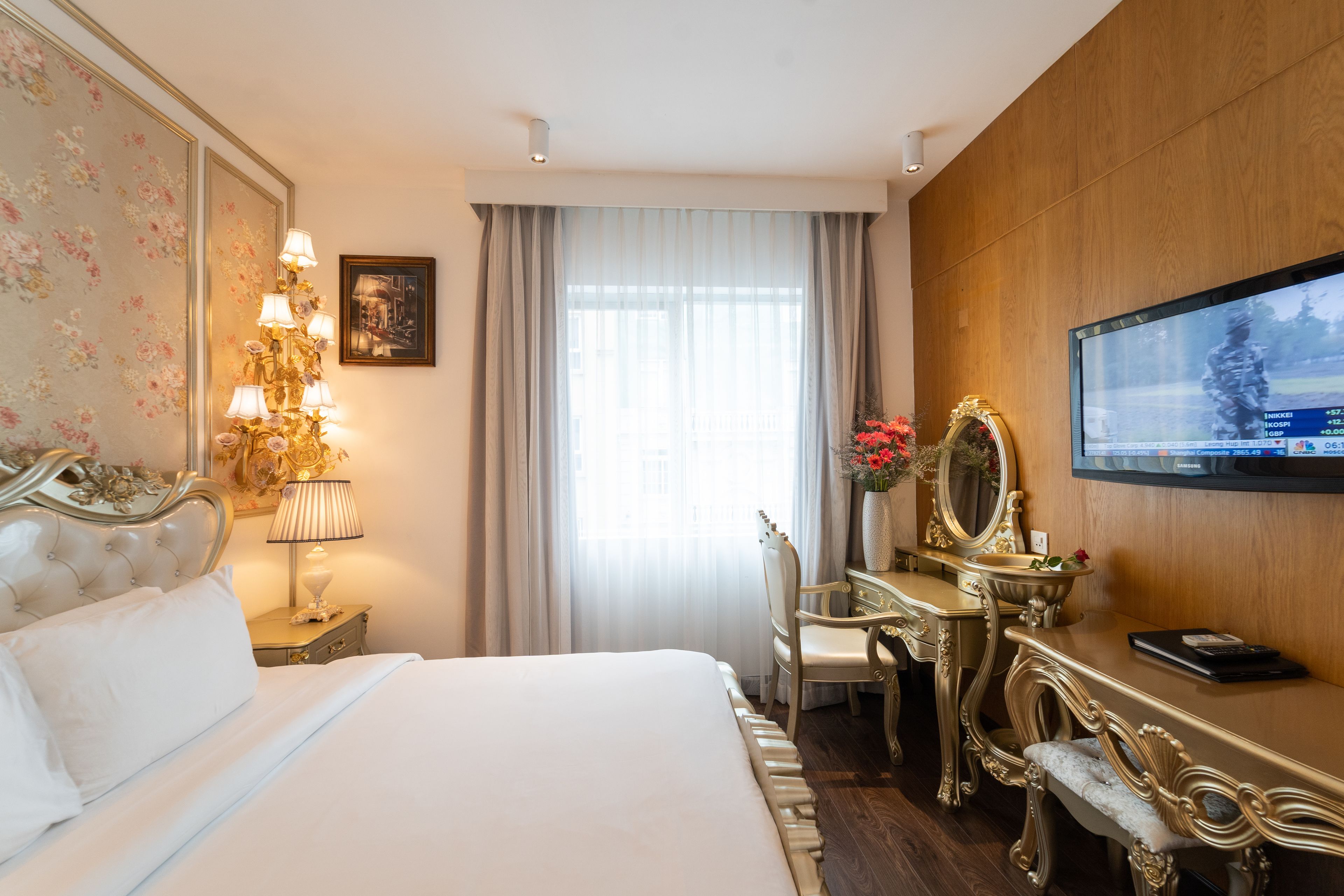 Ein Hotelzimmer mit einem großen Bett, einem Schreibtisch mit Spiegel, einem Fernseher und einer Chandelüster.