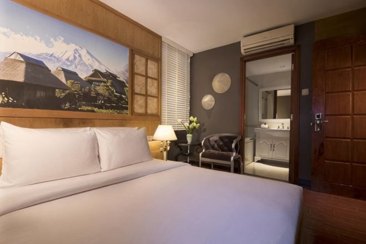 A hotel room with a bed, a painting of a mountain, a chair, a lamp, and a mirror.