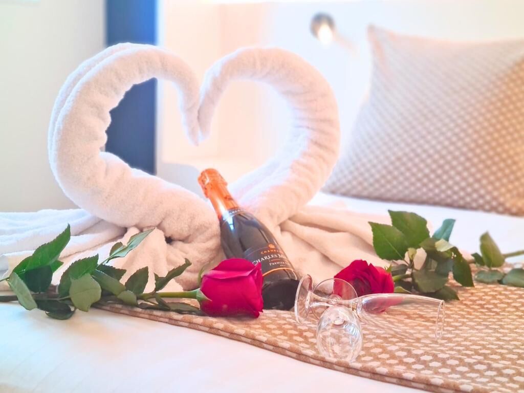 A bed with a heart-shaped towel arrangement, a bottle of champagne, and red roses.