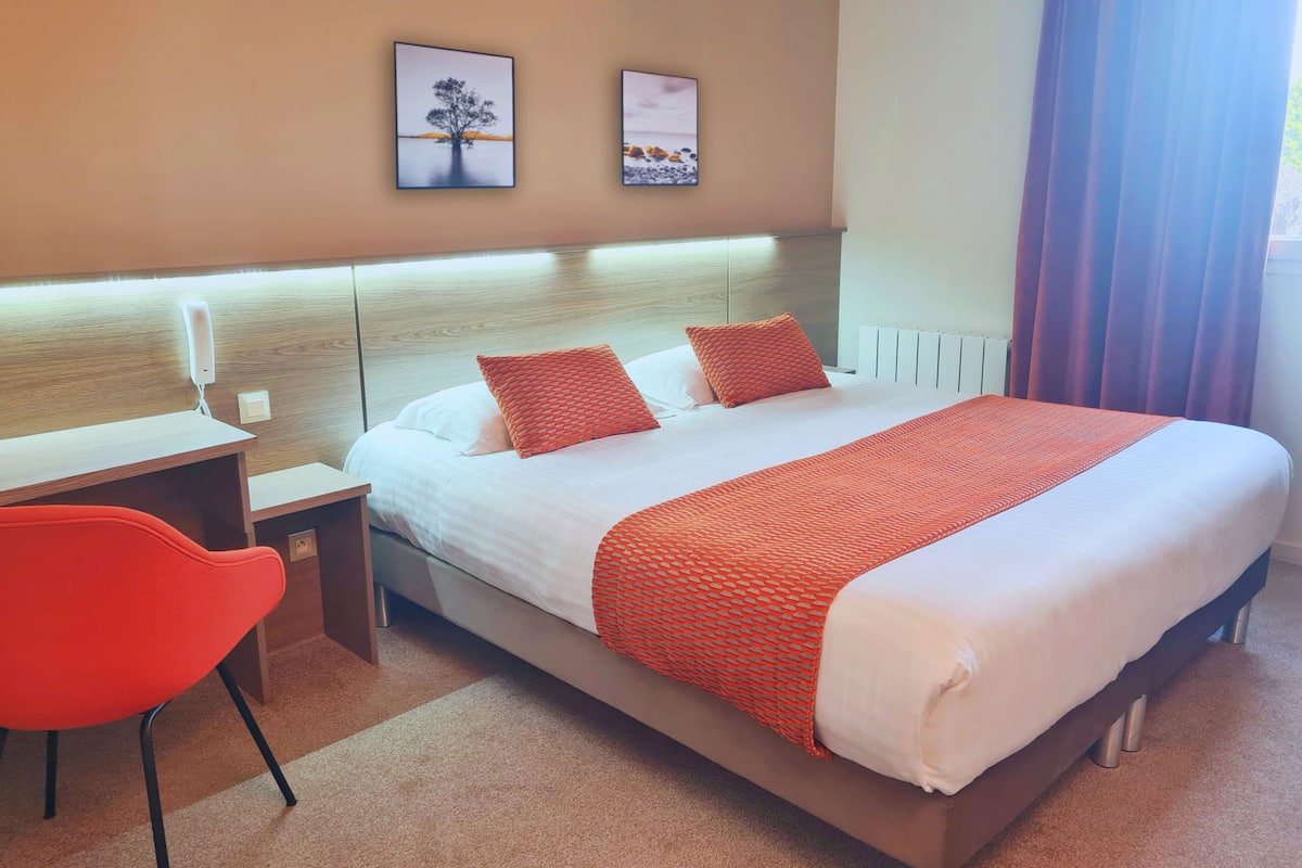 A hotel room with a bed, a desk, a chair, and two framed pictures on the wall.