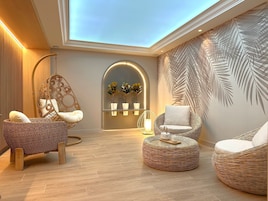 Un salón moderno con muebles de mimbre, una silla colgante y una pared con diseño de hojas de palmera.
