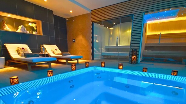 Un moderno espacio de spa con hidromasaje, sillones reclinables y ducha envuelta en vidrio.