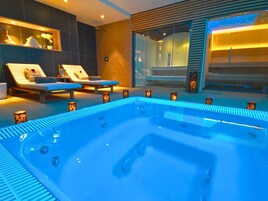 Un moderno espacio de spa con hidromasaje, sillones reclinables y ducha envuelta en vidrio.