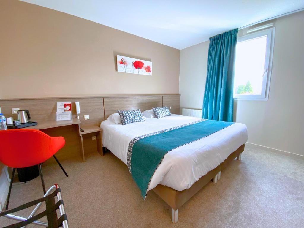 Habitación de hotel con cama, escritorio, silla, ventana con cortinas y una obra de arte en la pared.