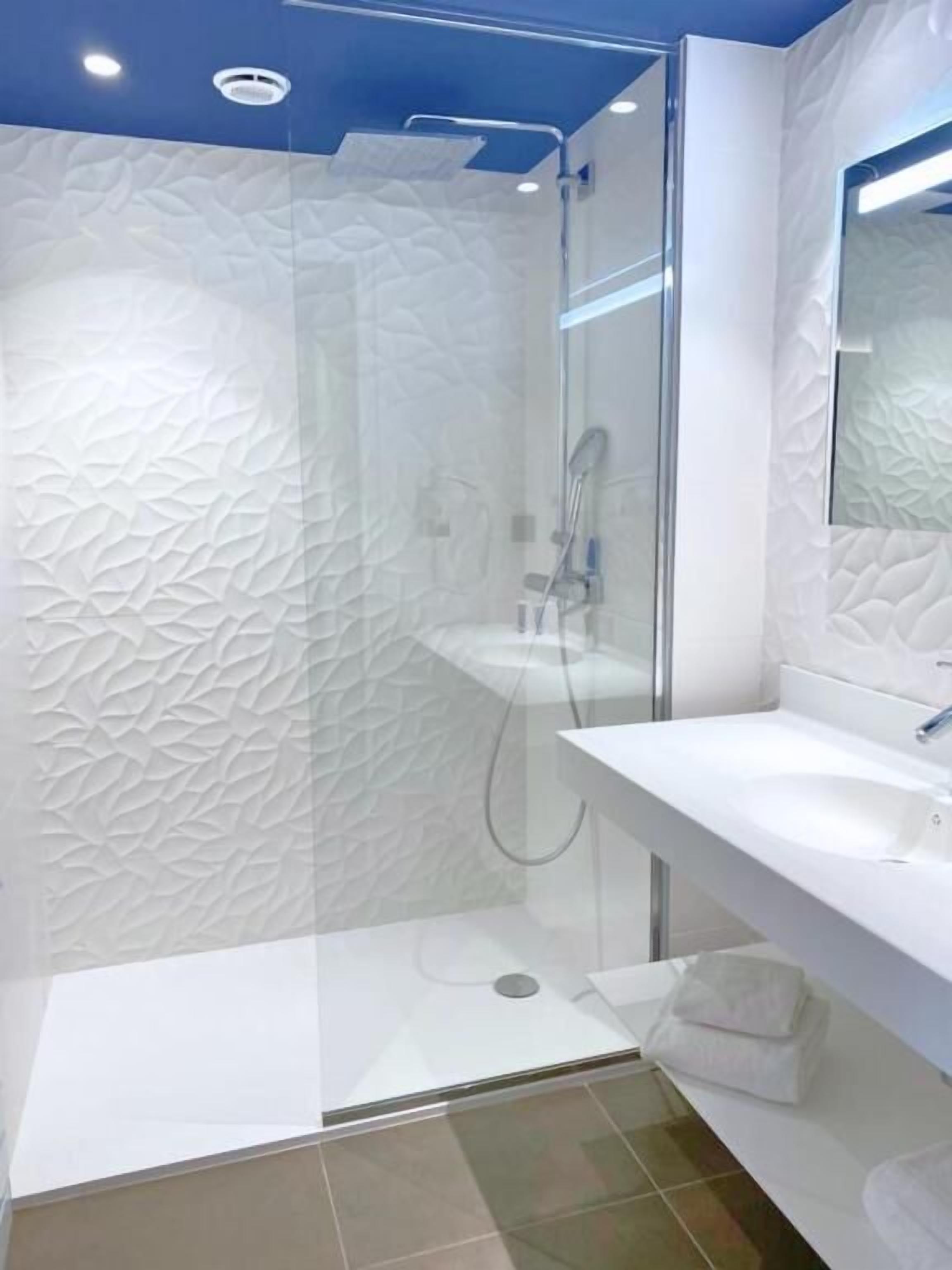 A modern bathroom with a glass shower enclosure, a white sink, and a mirror.
