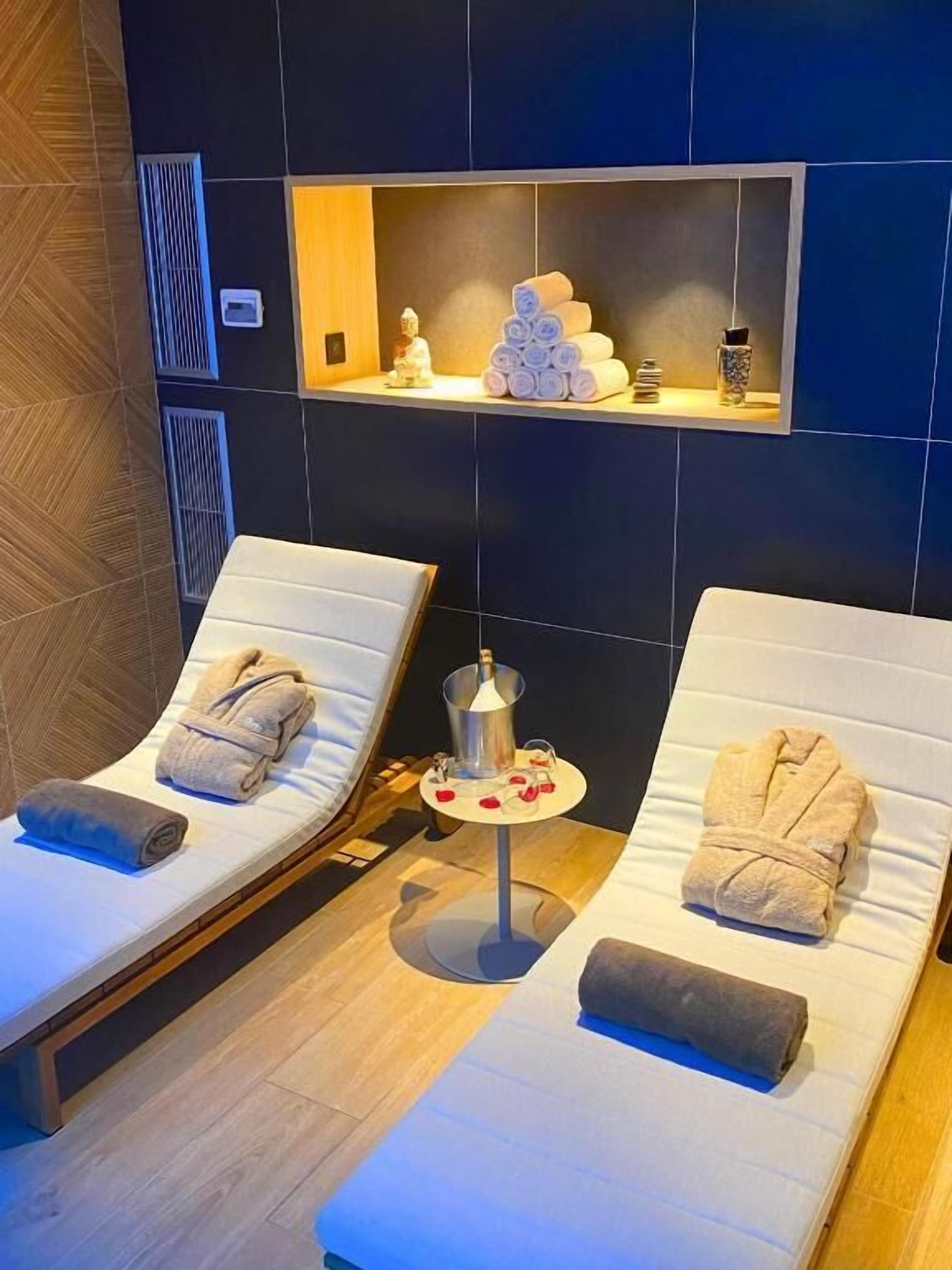 Een spa-ruimte met twee comfortstoelen, een tafeltje met een fles en een glas, en een plank met handdoeken en een decoratief object.