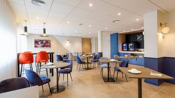 A modern restaurant with multiple tables and chairs, a kitchen area, and a staircase leading to an upper level.