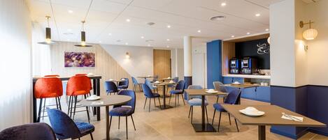 A modern restaurant with multiple tables and chairs, a kitchen area, and a staircase leading to an upper level.