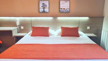 Habitación de hotel con una cama, dos almohadas, una mesita de noche, un teléfono y dos cuadros en la pared.