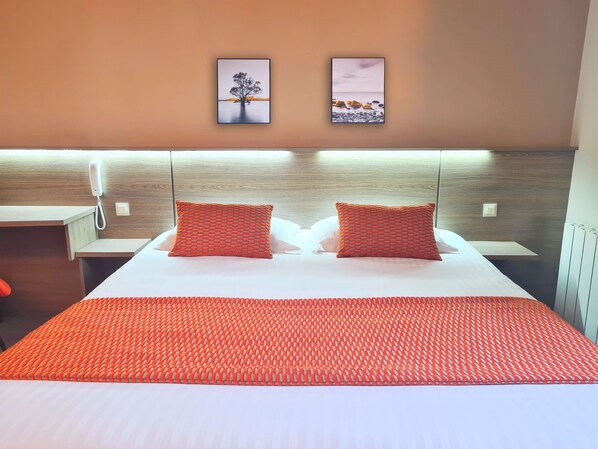 A hotel room with a bed, two pillows, a nightstand, a phone, and two framed pictures on the wall.