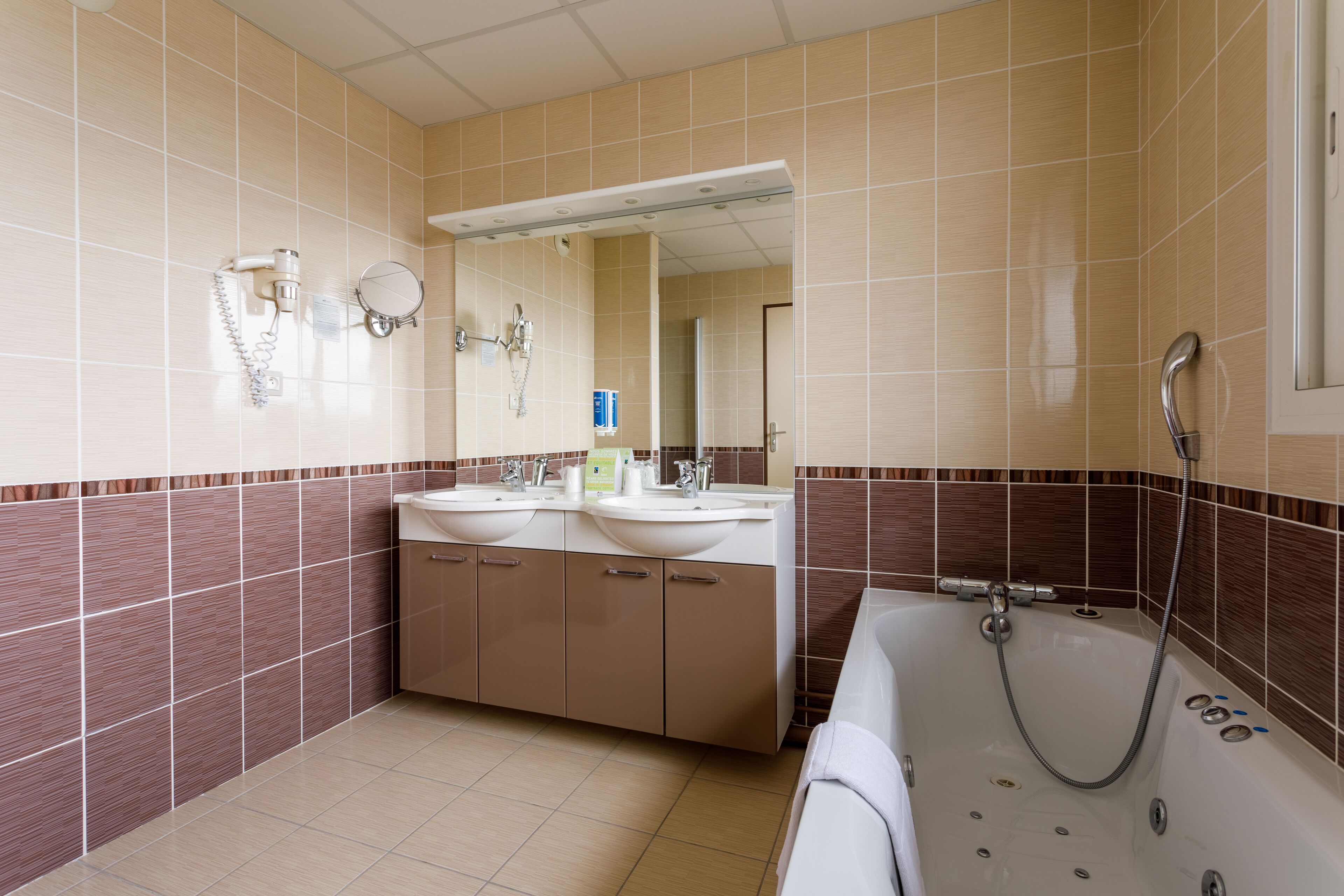 Un baño con dos lavamanos, un espejo grande, una bañera y paredes de azulejos.
