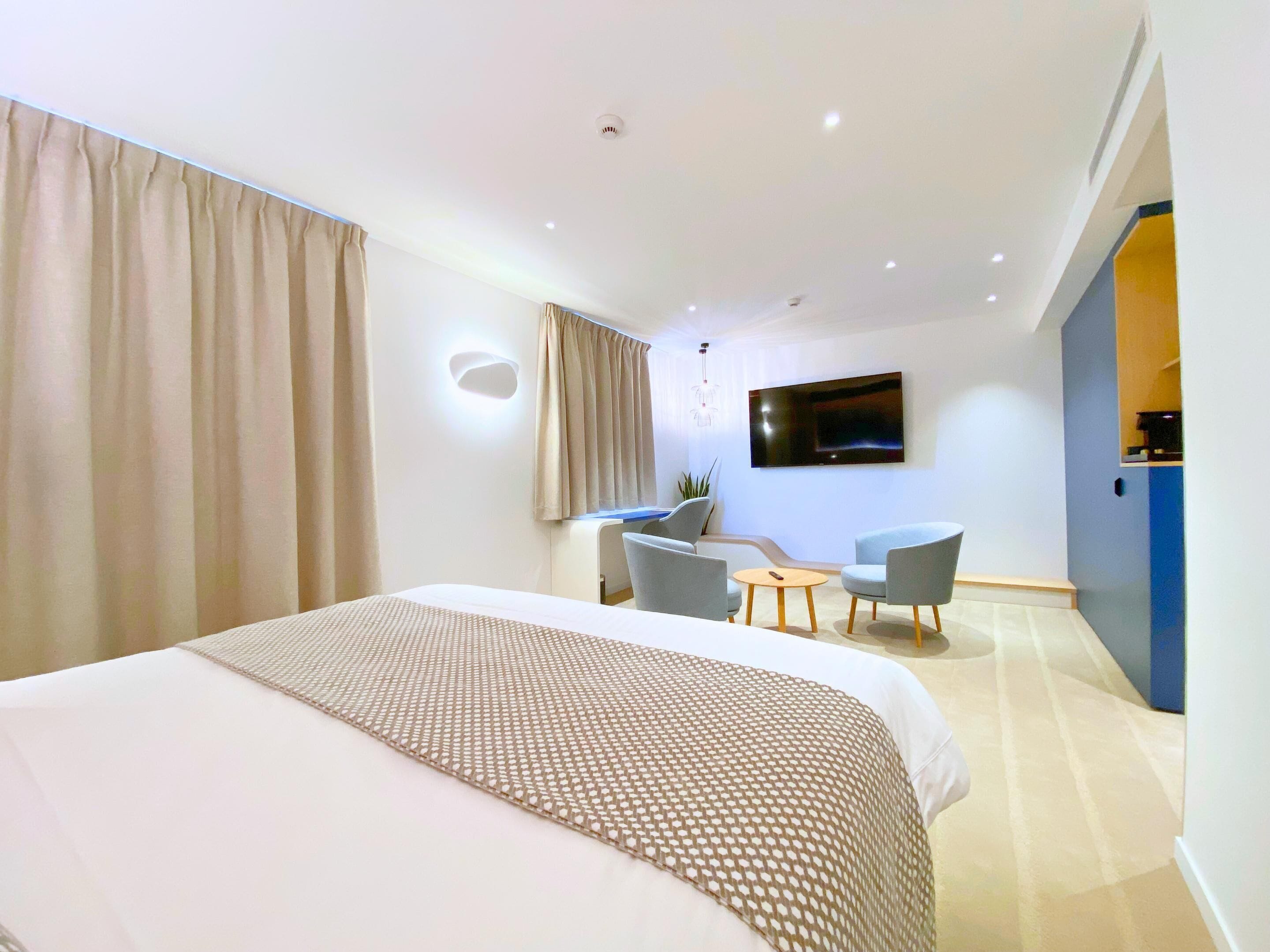 A modern hotel room with a large bed, a desk, two chairs, a TV, and a small table.