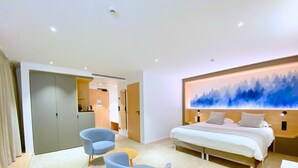 Una habitación de hotel moderna con una cama grande, un escritorio, dos sillas y un cuadro en la pared.