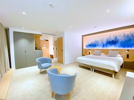 Una habitación de hotel moderna con una cama grande, un escritorio, dos sillas y un cuadro en la pared.
