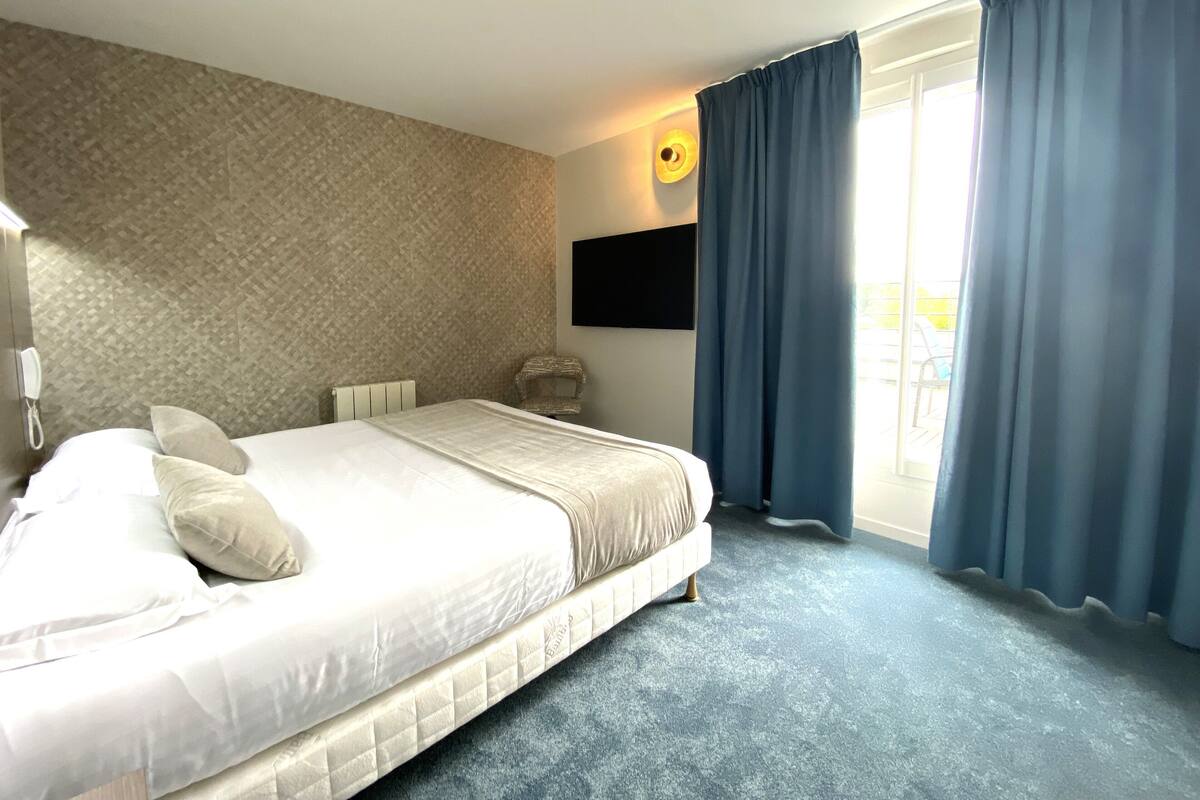 A hotel room with a large bed, a flat-screen TV mounted on the wall, and a window with curtains.