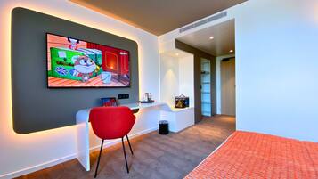 Una habitación moderna con una televisión de pantalla plana en la pared, una silla roja, un escritorio blanco y piso alfombrado.