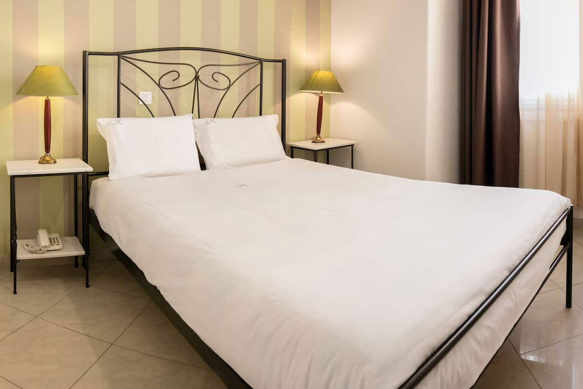 A neatly made bed with white linens, two bedside lamps, a bedside telephone, and a striped wall in the background.