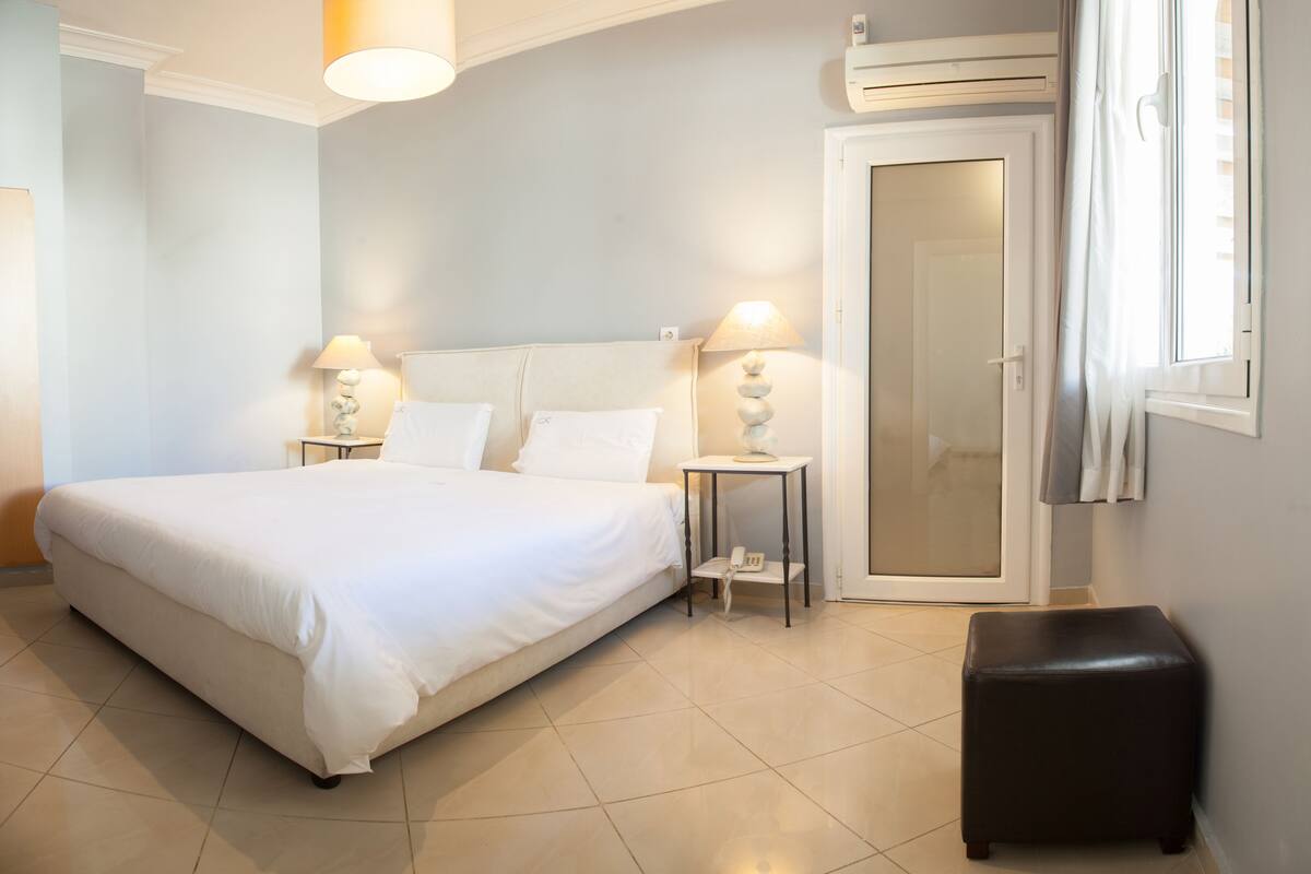 A neatly arranged bedroom with a large bed, bedside lamps, a small table, a door, and a window with curtains.