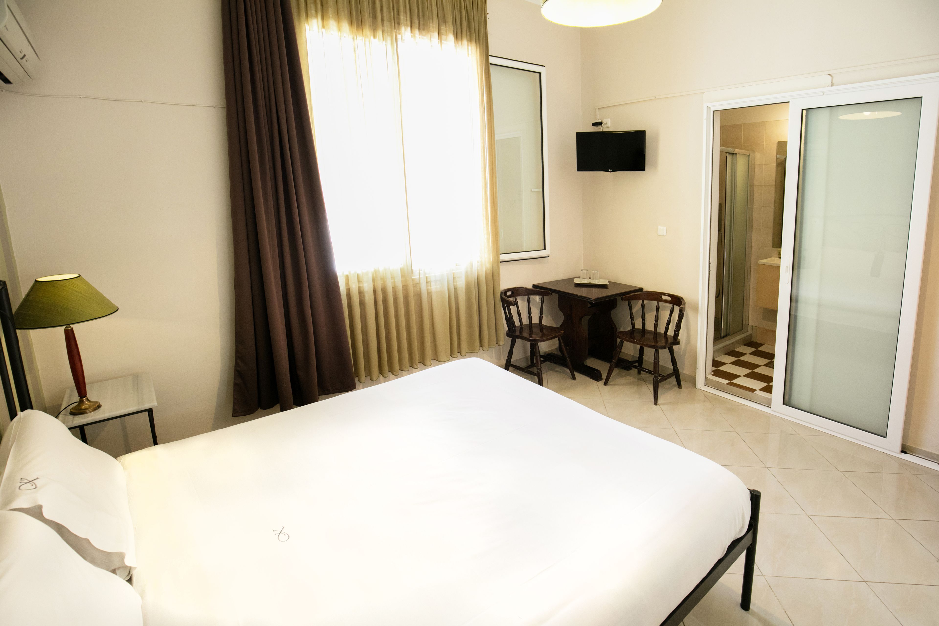 Ein Hotelzimmer mit einem Bett, einem Schreibtisch mit zwei Stühlen, einem Fernseher und einer Schiebetür zu einem Badezimmer.