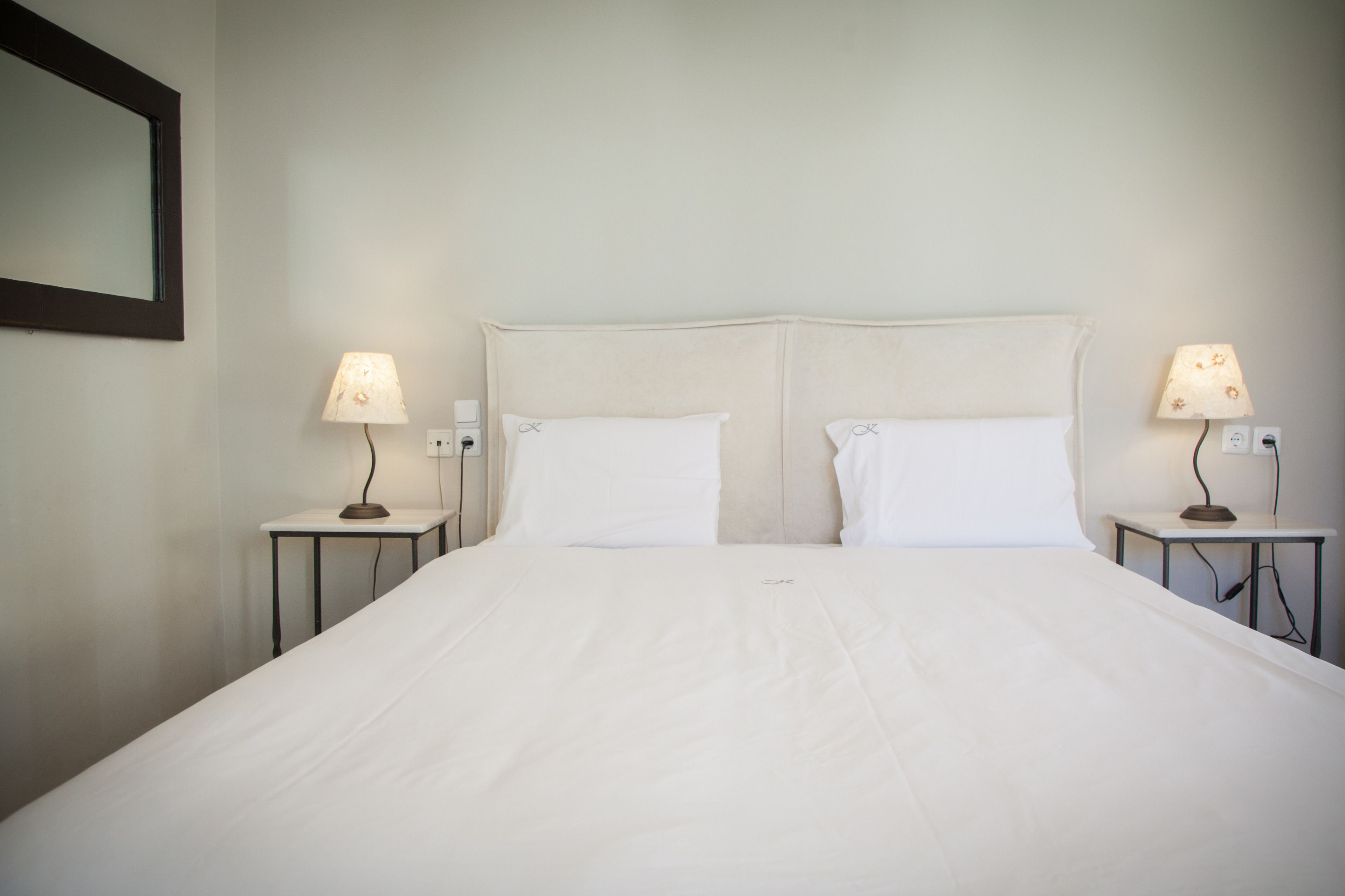 Ein Hotelzimmer mit einem großen Bett, zwei Nachttischen mit Lampen und einem Spiegel an der Wand.