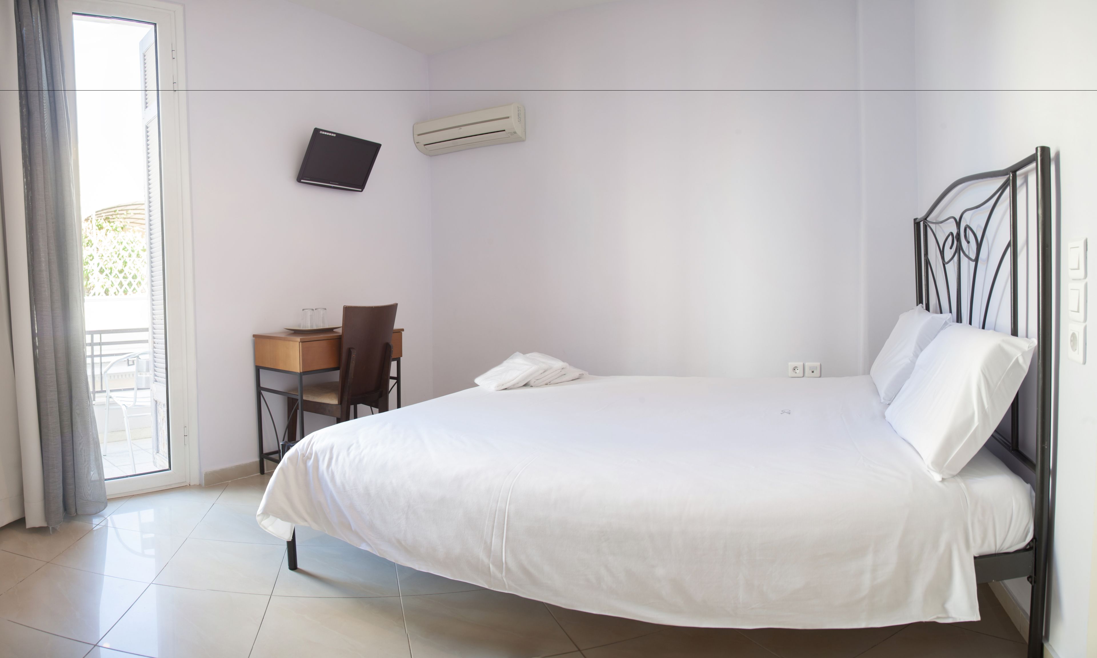 A bedroom with a bed, a desk with a chair, an air conditioner, and a window with curtains.
