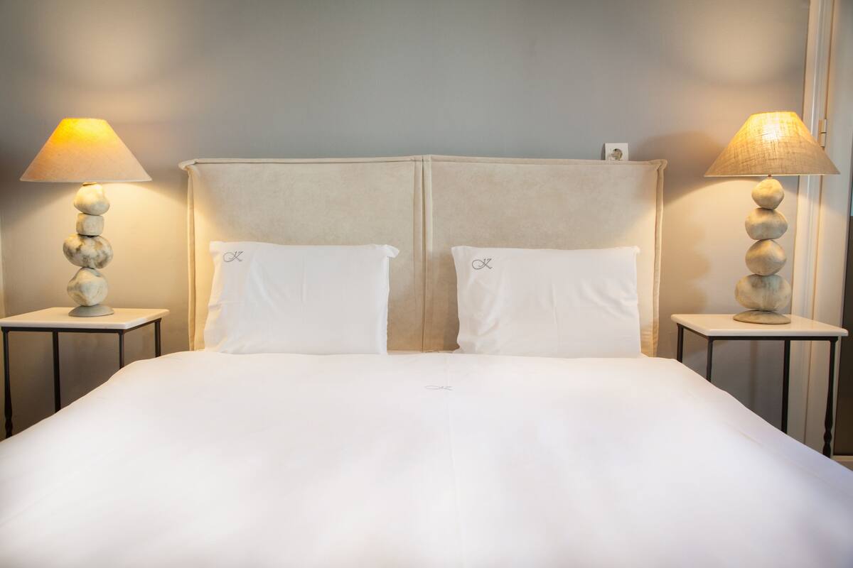 A double bed with a headboard, two bedside lamps, and a small table with a lamp on each side.