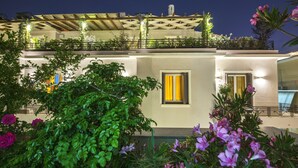 A modern building with a balcony, a window with yellow curtains, and a garden with purple flowers. - Kimon Athens Hotel (Athens)