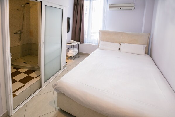 A hotel room with a large bed, a shower area, and a small table with a phone.