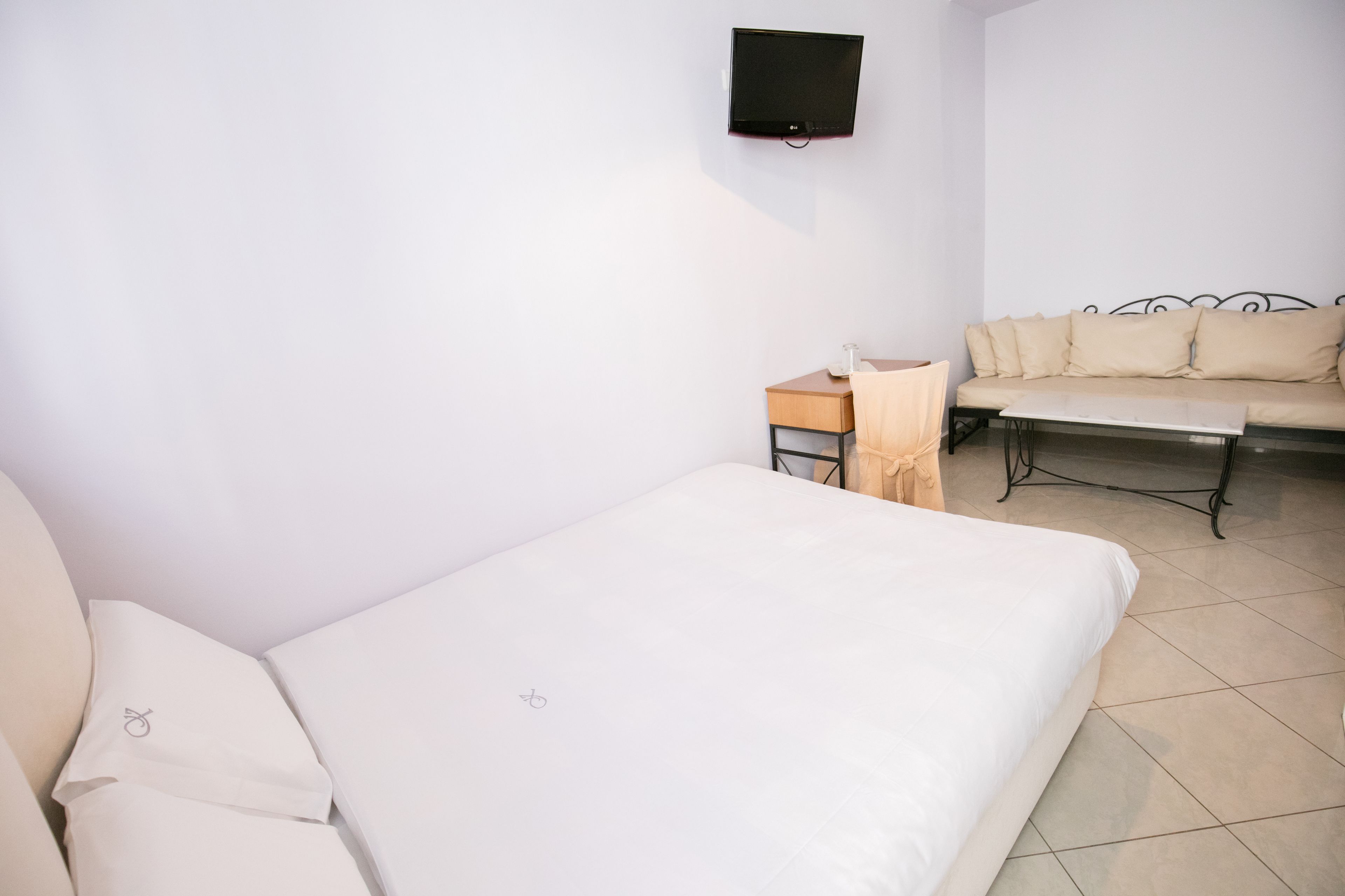 Une chambre avec un lit, un canapé, un téléviseur fixé au mur et une petite table.