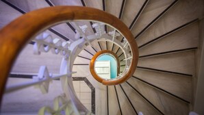 A spiral staircase with a wooden handrail and white railings, leading to an open area with a view of the sky. - Kimon Athens Hotel (Athens)