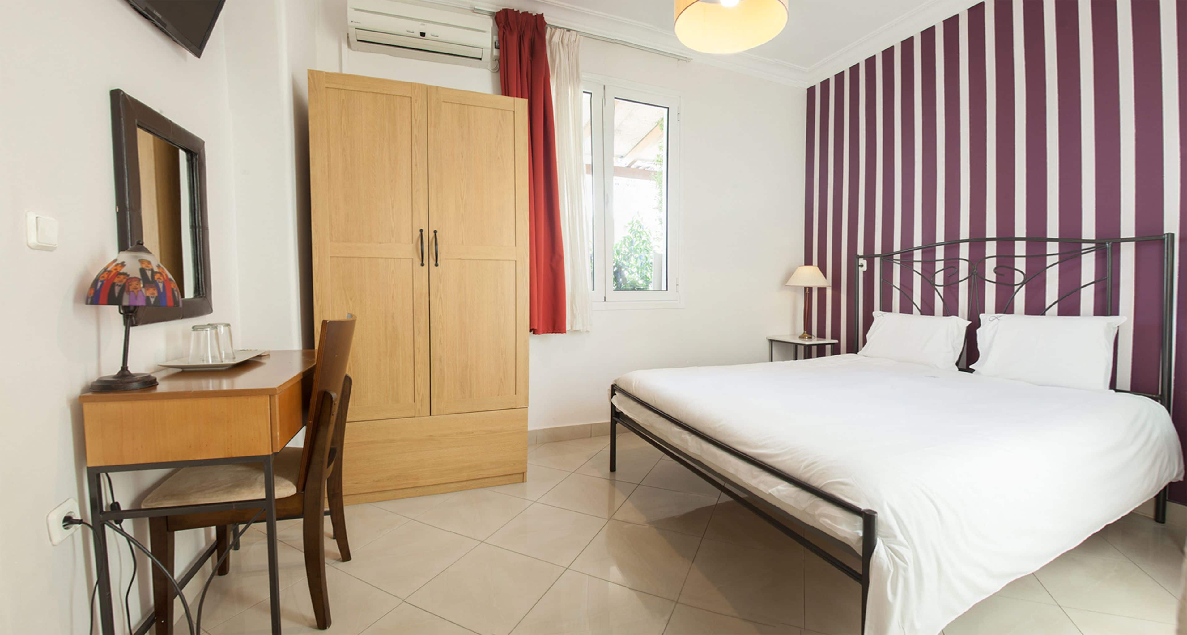Une chambre à coucher comprenant un lit, un bureau, une chaise, une armoire et une fenêtre avec des rideaux.
