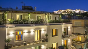 A multi-story building with balconies, large windows, and a view of a hill with buildings in the background. - Kimon Athens Hotel (Athens)