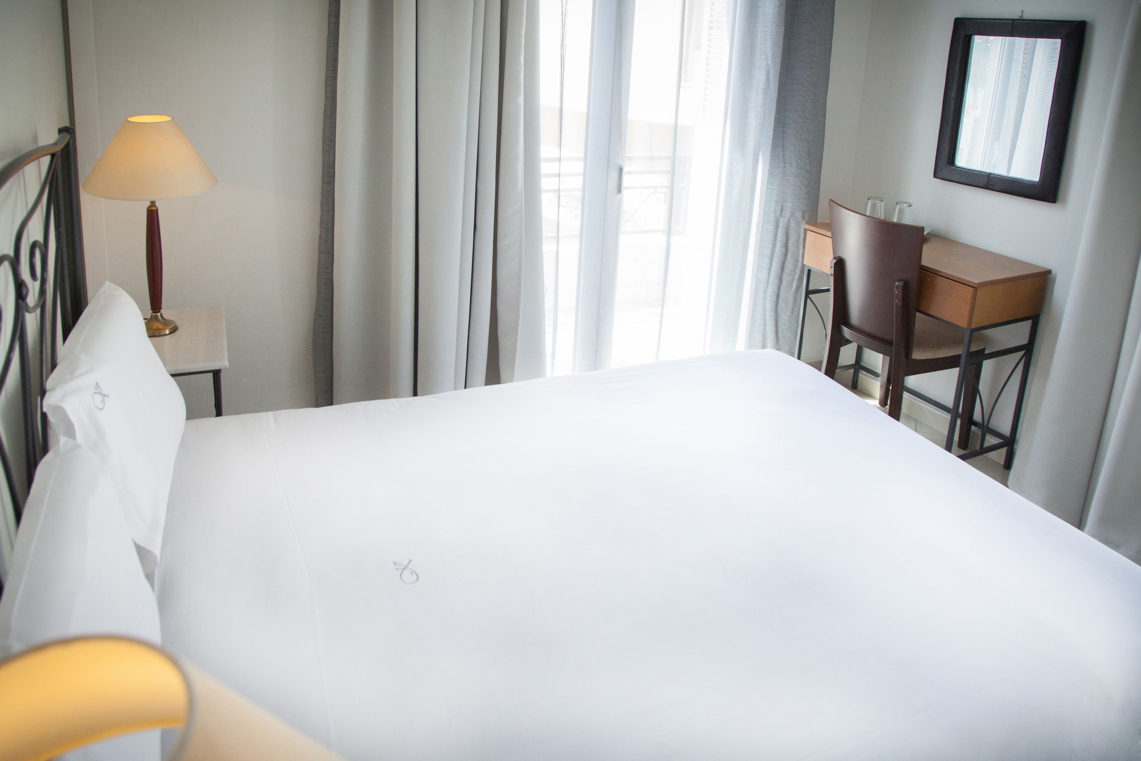 A hotel room with a bed, a desk, a chair, a lamp, and a window with curtains.
