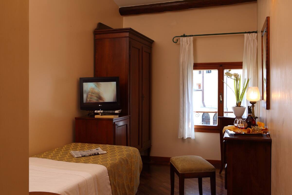 A hotel room with a bed, a television, a desk with a lamp, and a window with curtains.