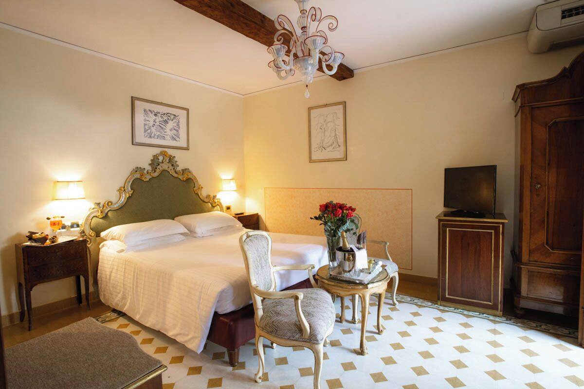 A hotel room with a bed, a chair, a small table with a vase of flowers, a television, and a wooden cabinet.