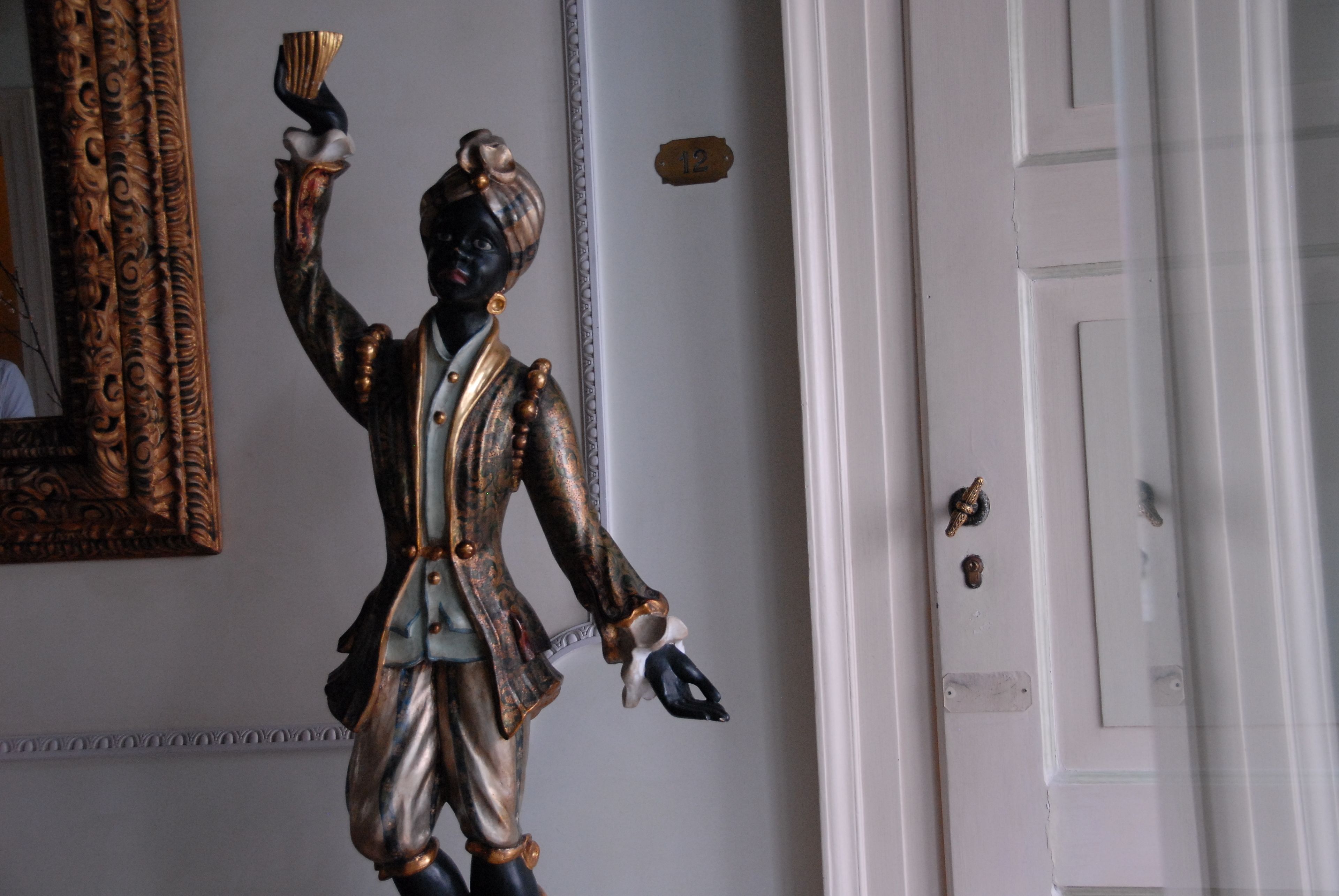 A statue of a person holding a cup, a door with a number plate, and a mirror with an ornate frame.