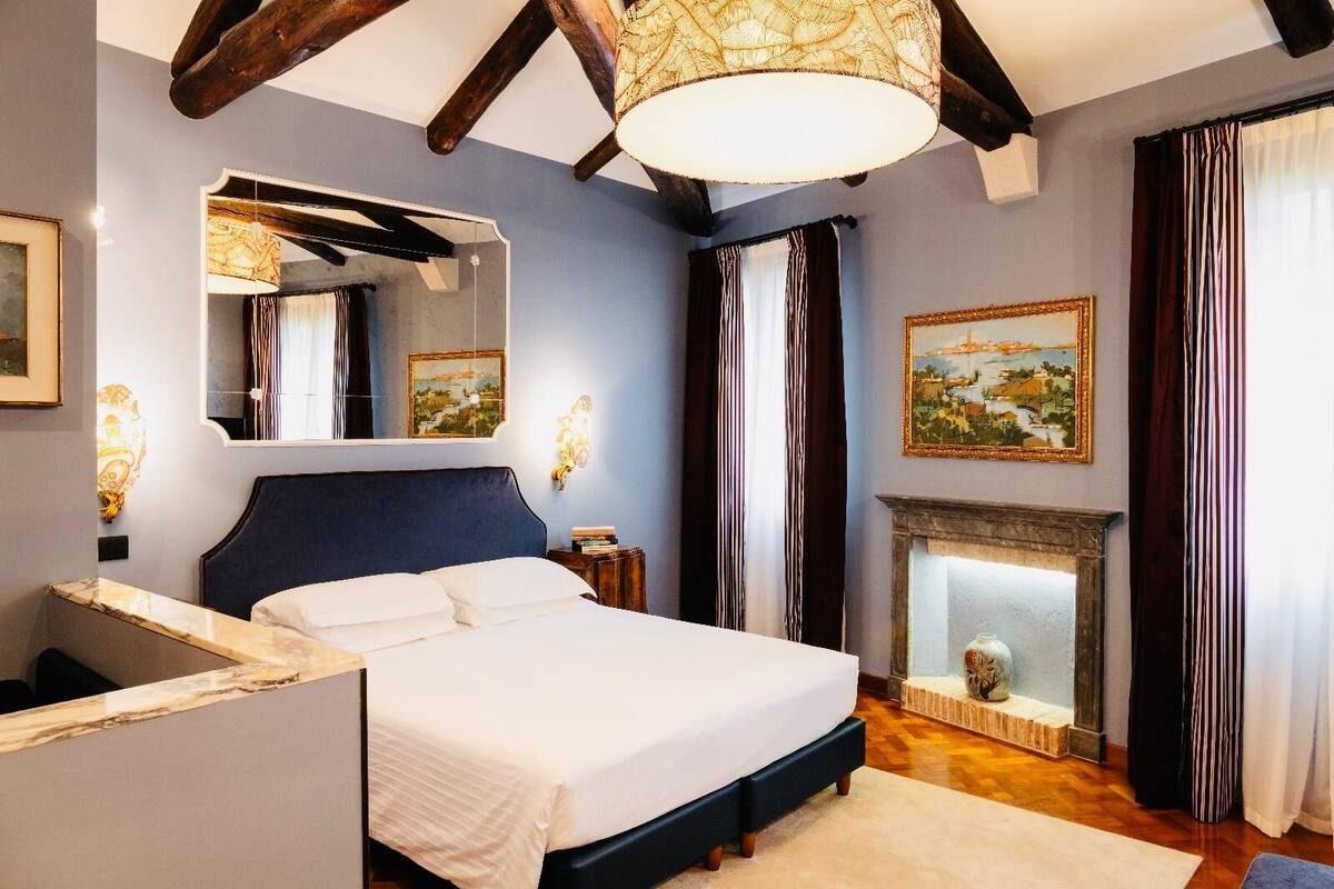 A bedroom with a large bed, a fireplace, a mirror, and a painting on the wall.