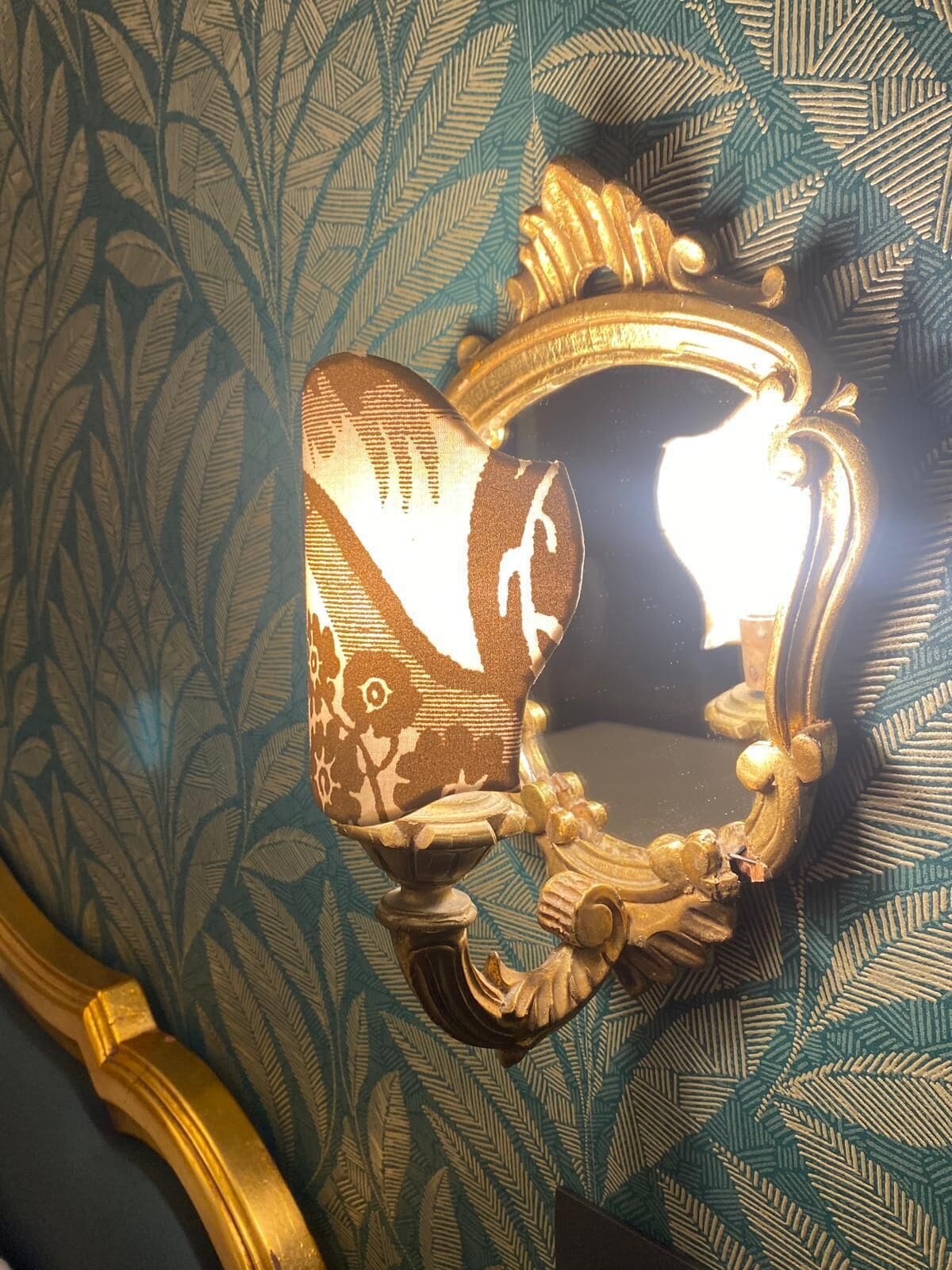 A wall sconce with a decorative design, mounted on a wall with a leaf-patterned wallpaper.