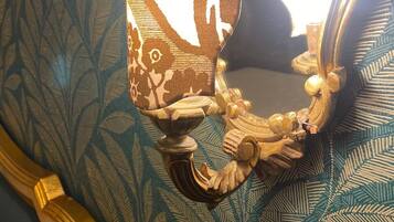A wall sconce with a decorative design, mounted on a wall with a leaf-patterned wallpaper.