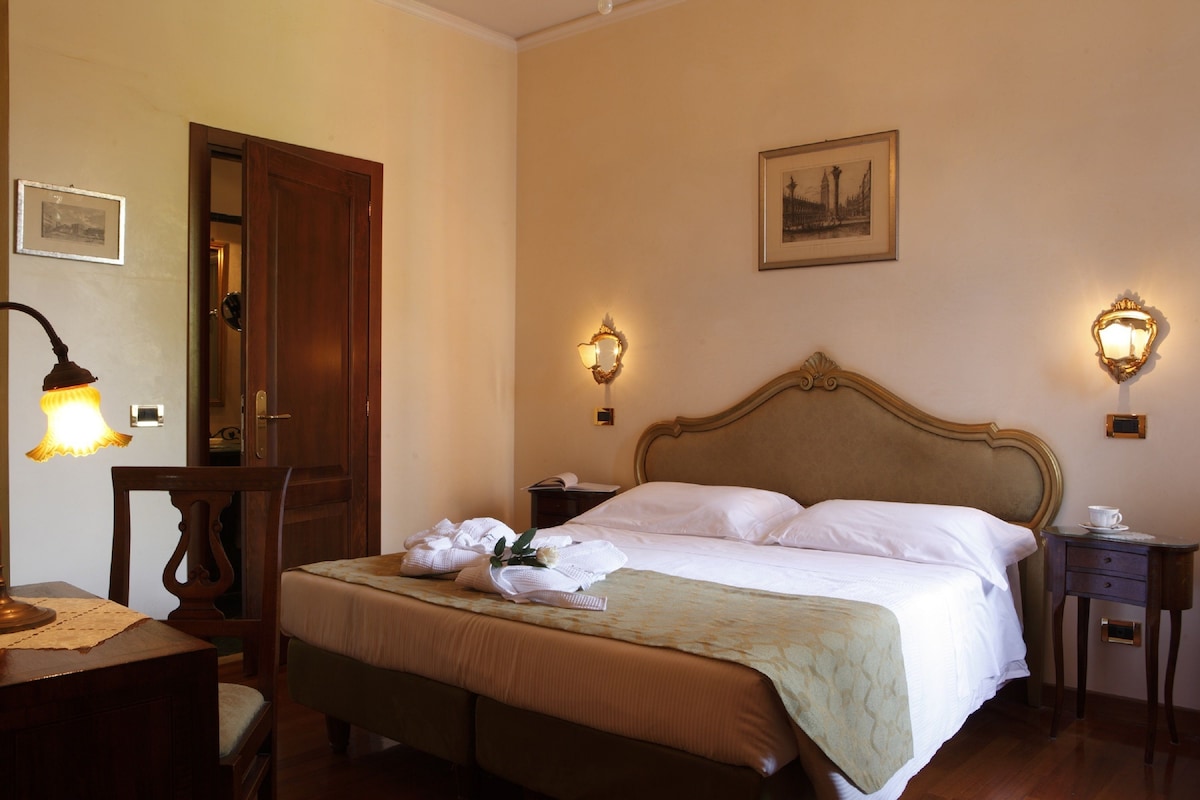 A hotel room with a bed, bedside tables, a lamp, and wall-mounted lights.