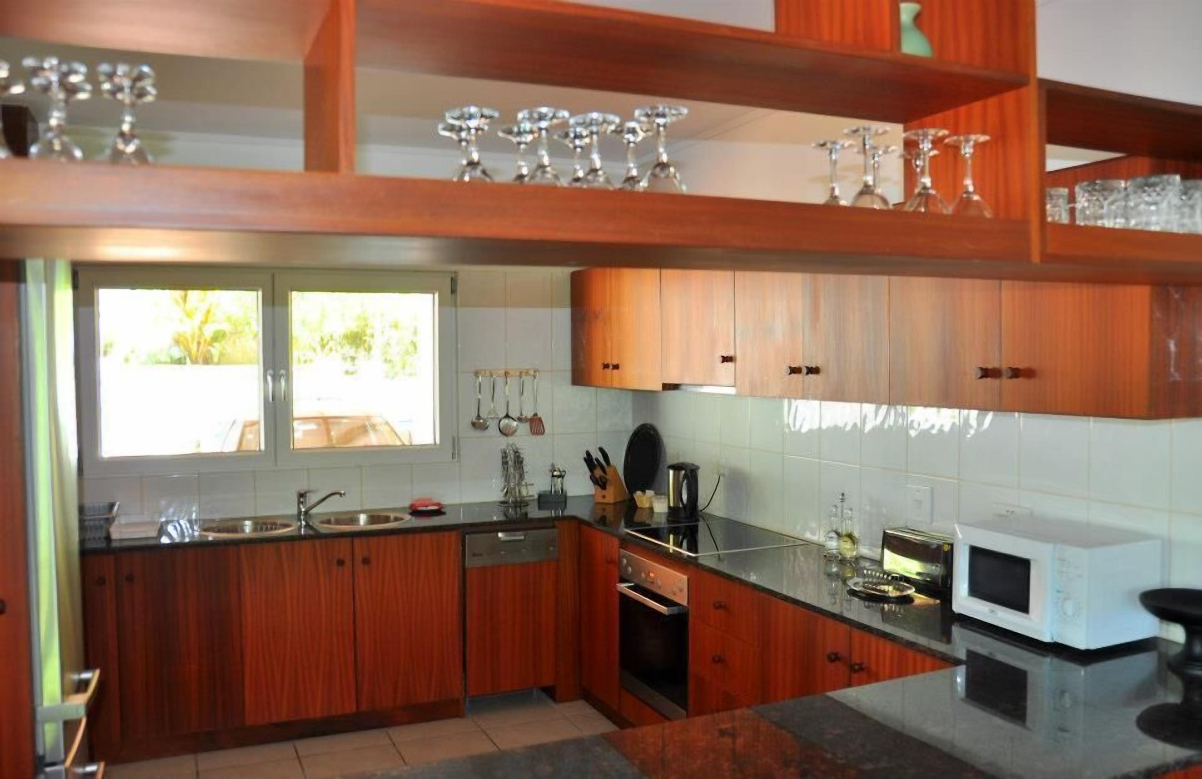 Une cuisine moderne avec des meubles en bois, un four encastré, un four à micro-ondes et une fenêtre qui laisse entrer la lumière naturelle.