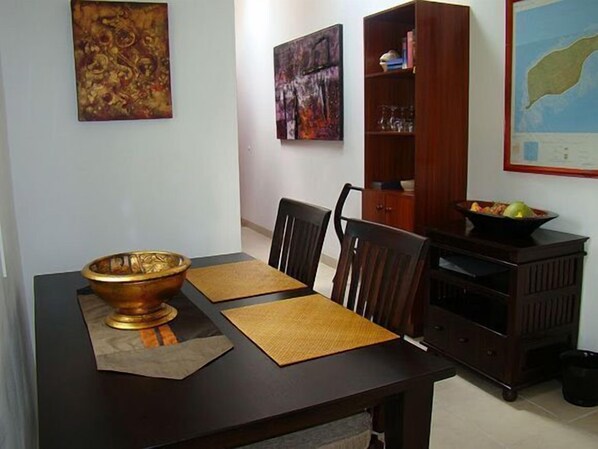 A dining area with a dark wooden table, four chairs, a large bowl, and two placemats. - Hanneman Holiday Residence (Mahé Island)